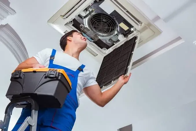 A technician servicing a commercial ceiling HVAC unit